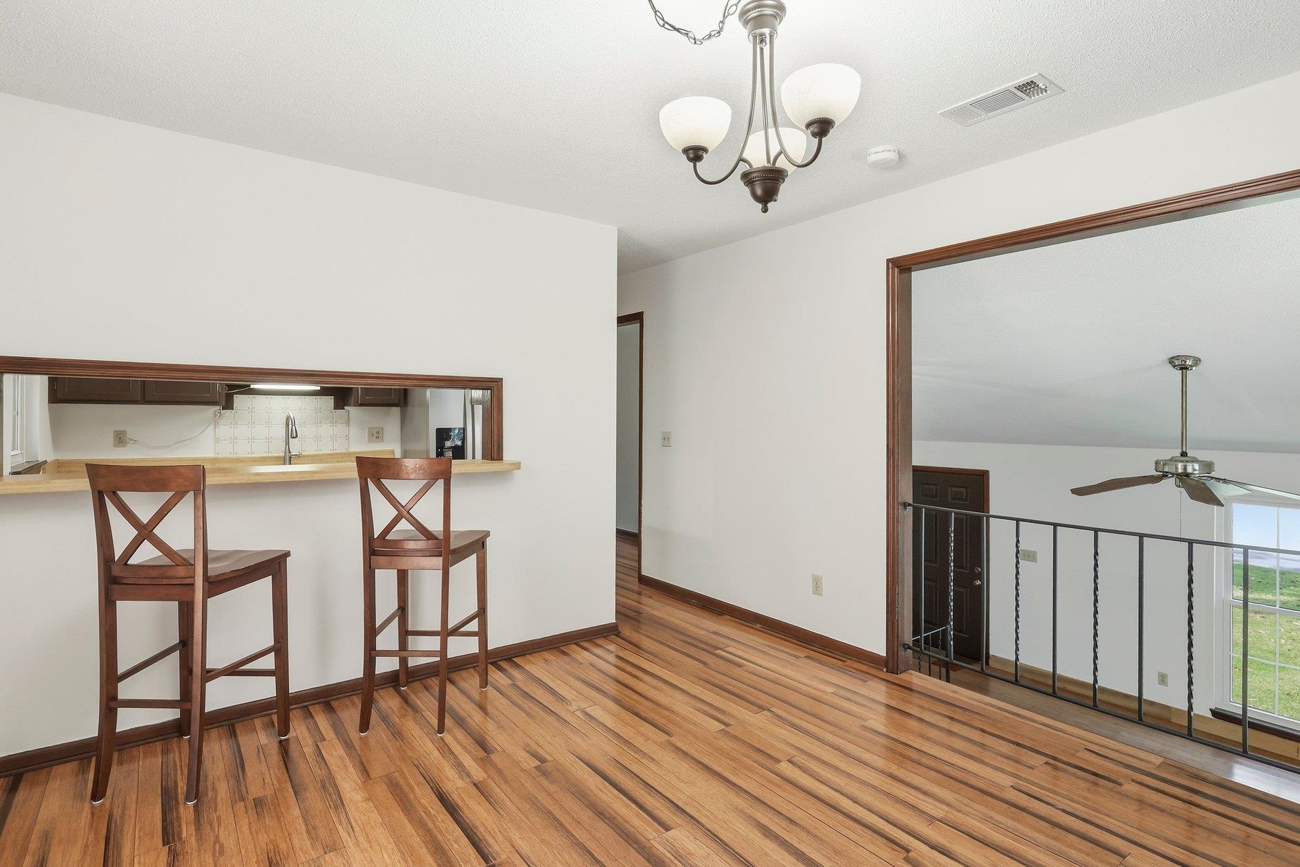 Upper-level room with a wood breakfast bar, two stools, hardwood floors, and an overlook railing.