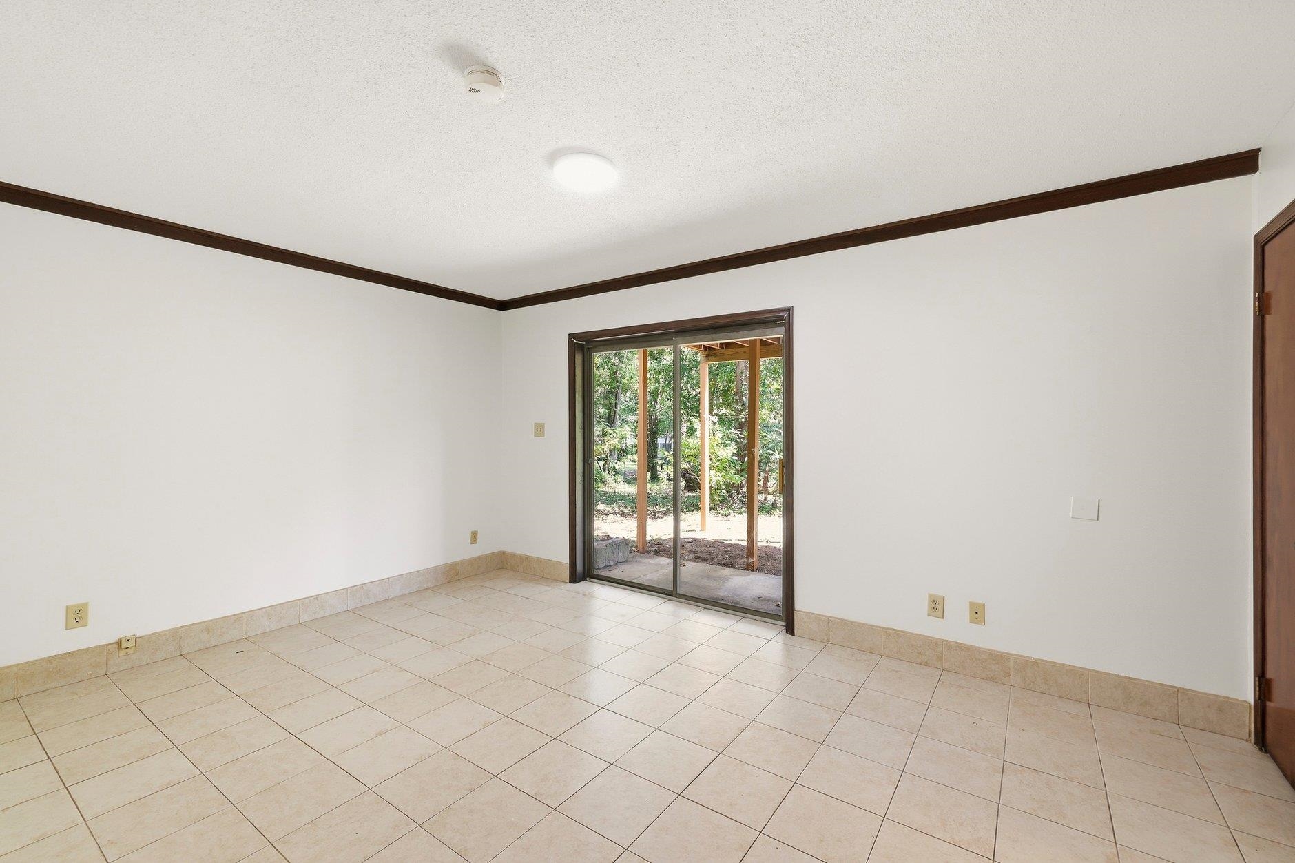Empty tiled room with dark wood trim and sliding glass doors to a covered patio.