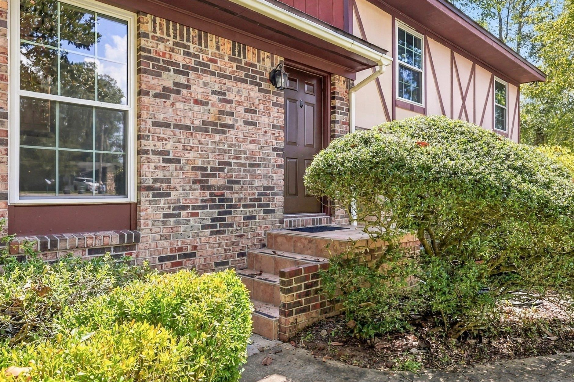 Home entrance with brick steps, dark front door, and trimmed shrubs.