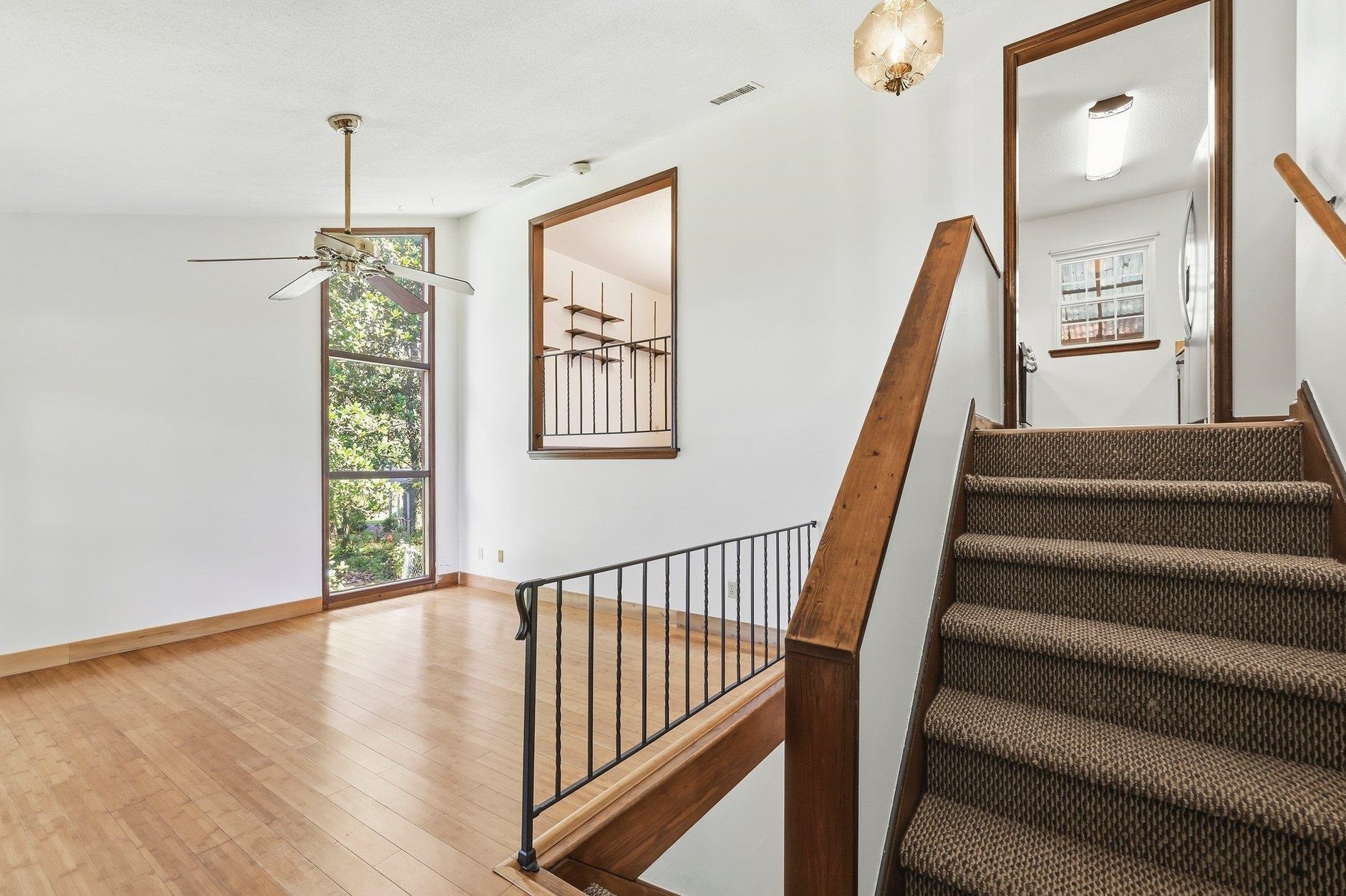Interior landing with tall window, wood floors, black railing, and carpeted staircase.