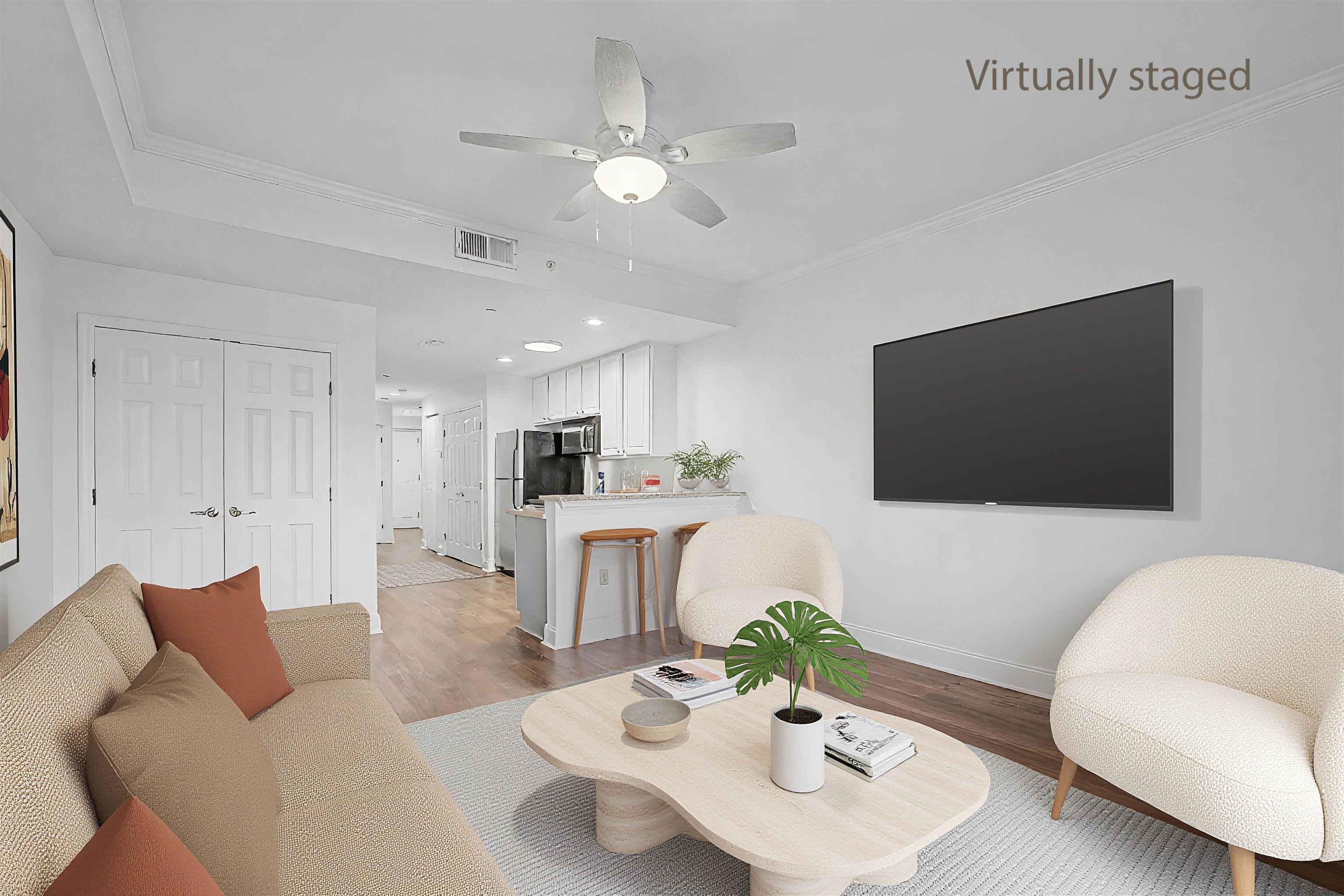 Virtually staged living room with a beige sofa, white chairs, and an open kitchen.
