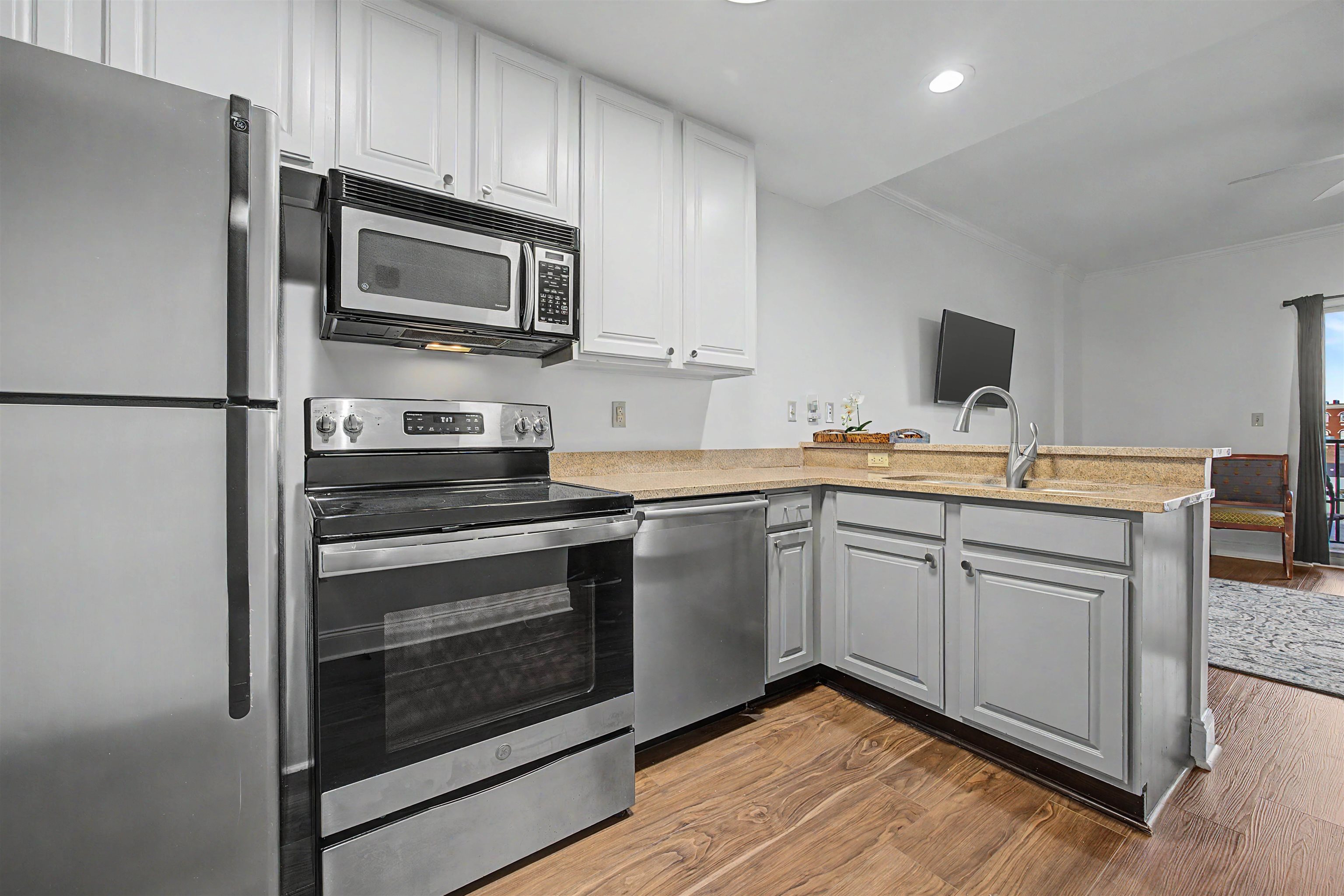 Condominium kitchen with white cabinets, stainless steel appliances, tan counters, and wood-look floors.
