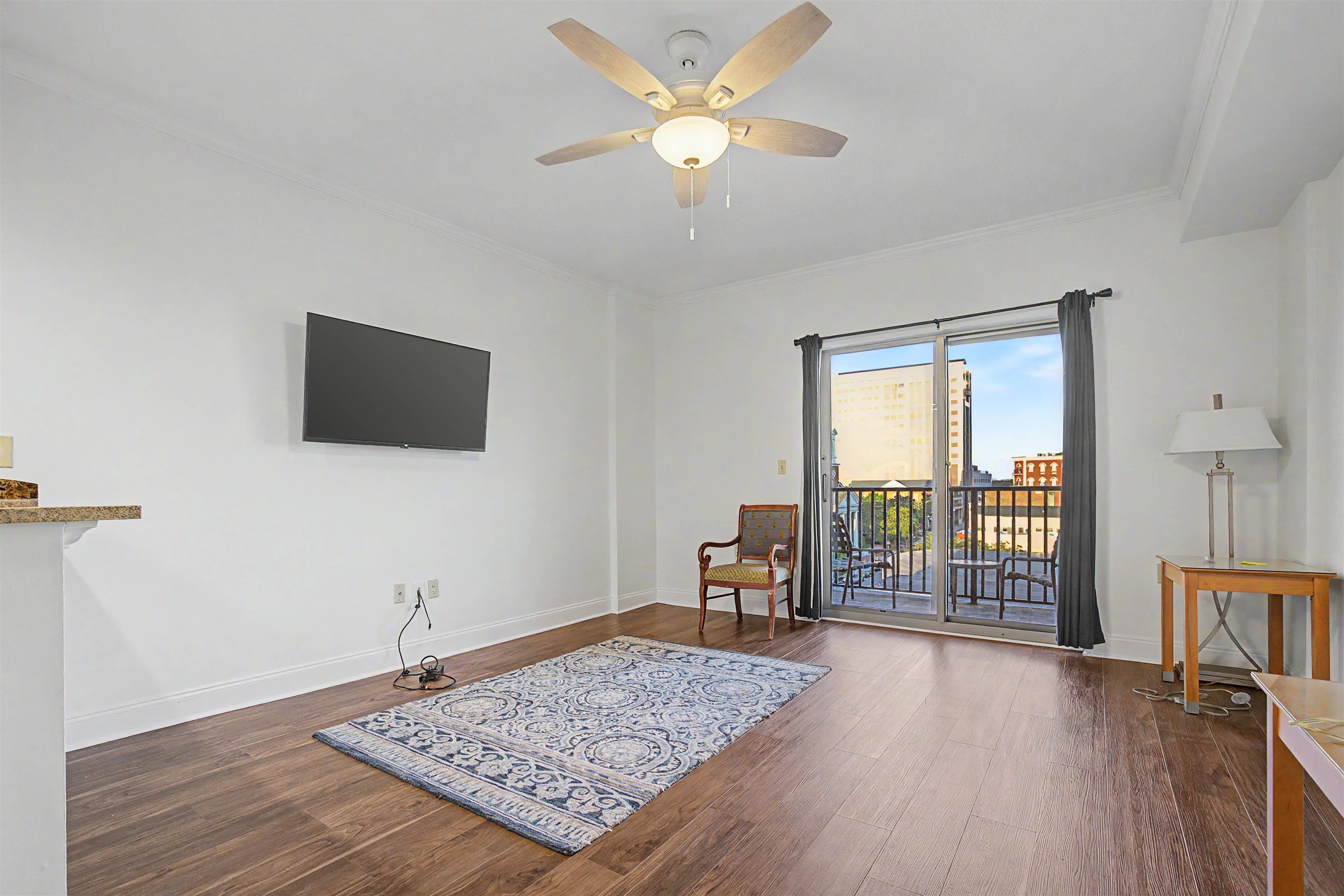 Living room with wood floors, ceiling fan, and sliding doors overlooking downtown from a balcony.
