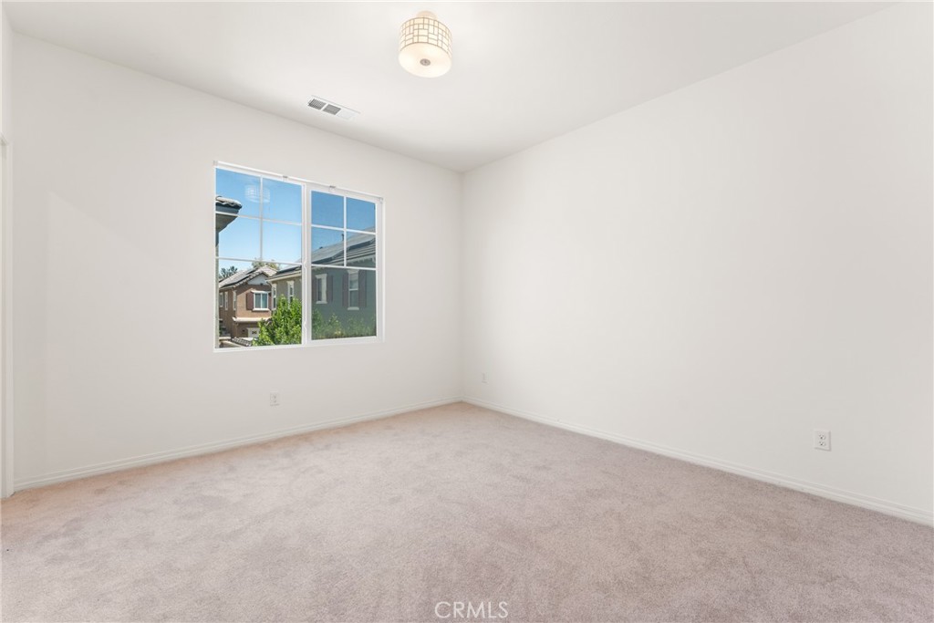 Empty bedroom with light carpeting and a large window overlooking neighboring homes.