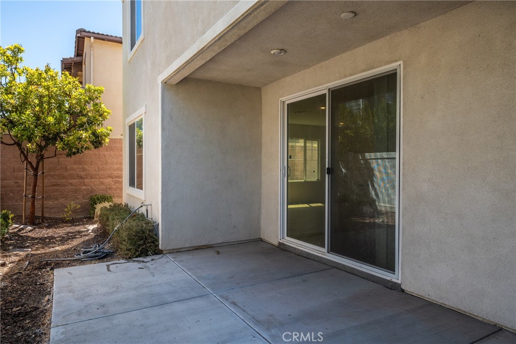 Covered concrete patio with a sliding glass door and landscaped side yard.