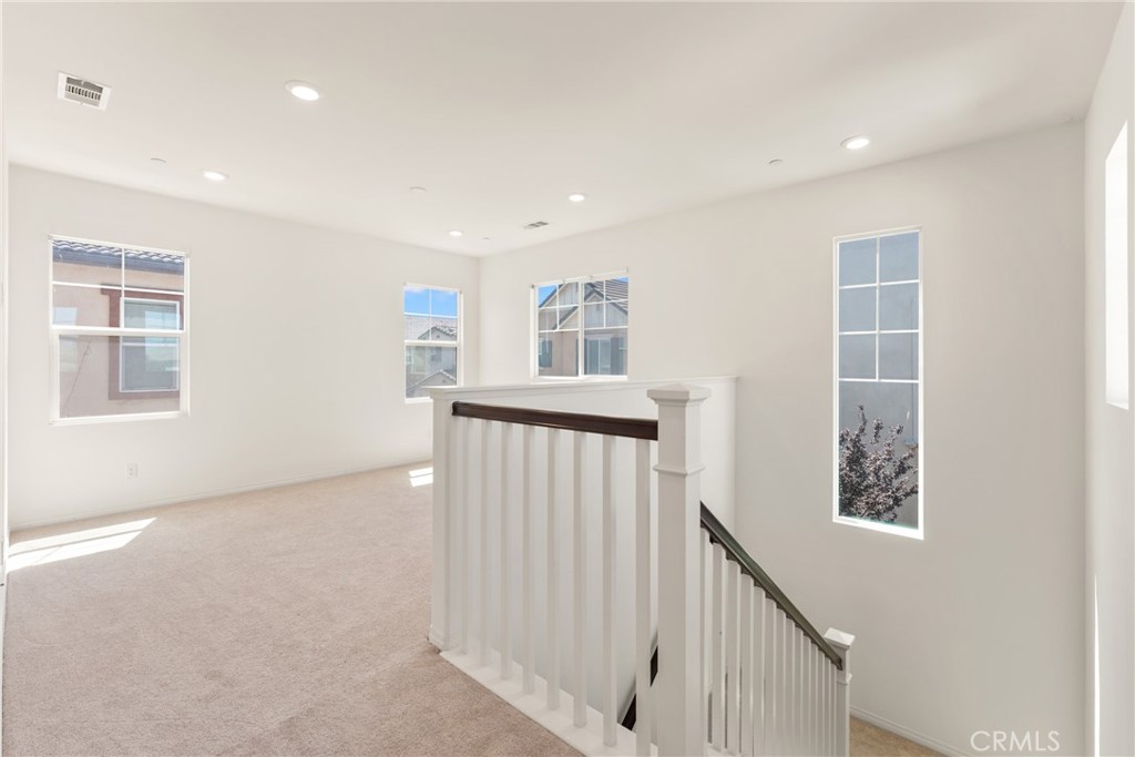 Carpeted upstairs landing with a white staircase railing and several windows.