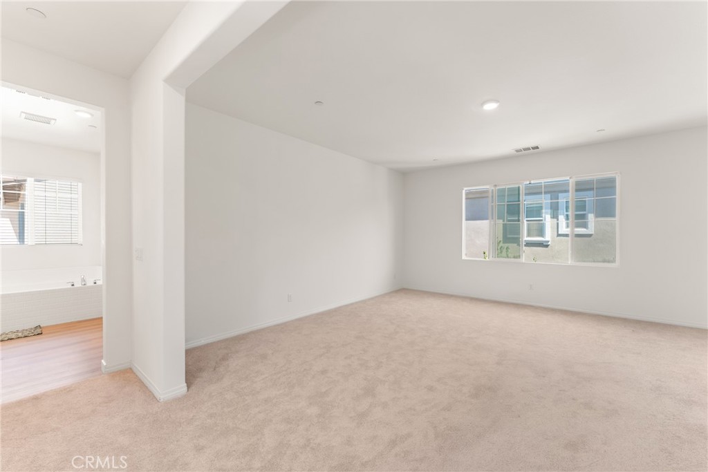 Empty carpeted bedroom with a wide window and an adjoining bathroom doorway.