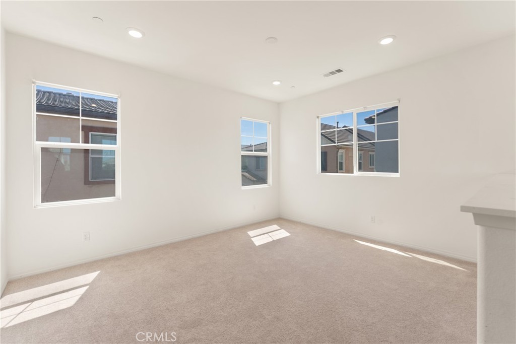 Vacant carpeted room with three windows and bright sunlight on the floor.