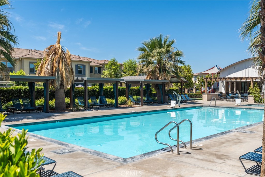 Community swimming pool with turquoise water, shaded pergolas, and palm trees.