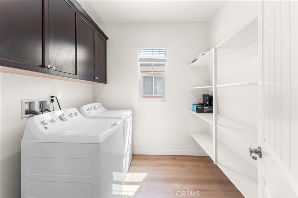 Laundry room with washer and dryer, dark cabinets, open shelving, and light wood flooring.
