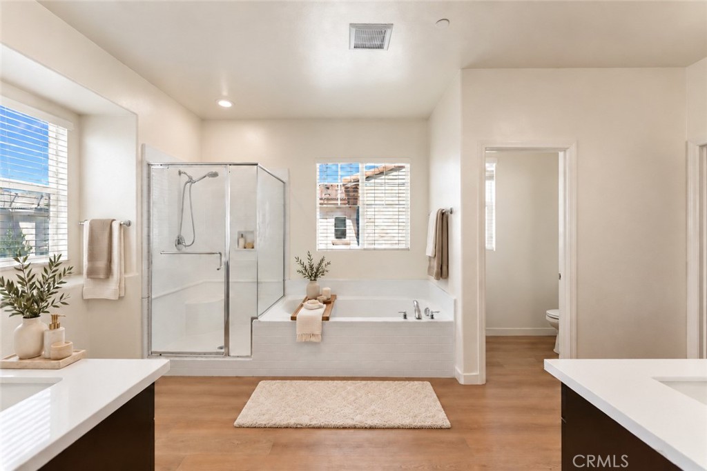 Bathroom with a glass shower, built-in tub, wide vanity counters, and wood flooring.