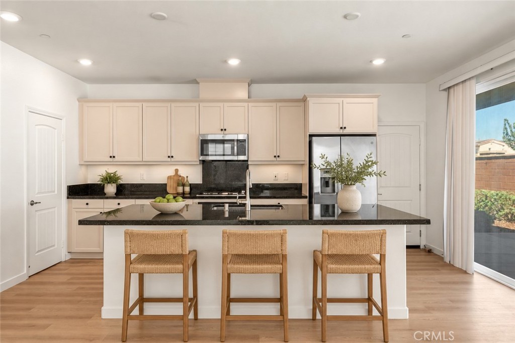 Staged kitchen with cream cabinets, black countertops, stainless appliances, and an island with three woven stools.