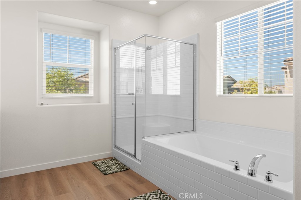 Bright bathroom with a white tub and glass shower enclosure between two windows.
