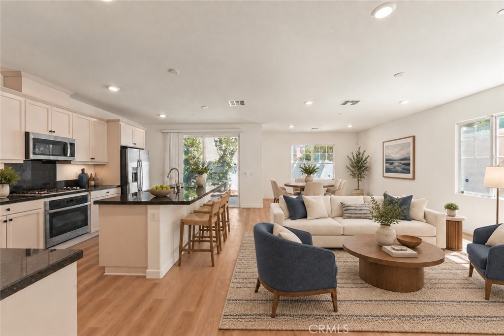 Open-plan living room with a cream sofa, blue chairs, and kitchen island with bar stools.