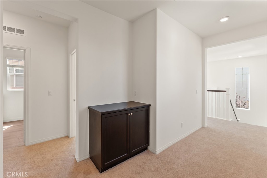 Carpeted upstairs hallway with a dark cabinet and openings to adjacent rooms.