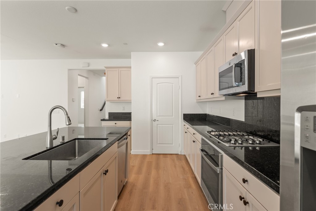 Vacant kitchen with black stone counters, light cabinets, and stainless steel appliances.