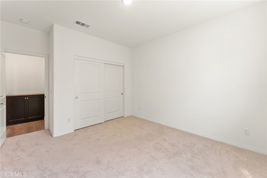 Empty bedroom with beige carpet, white sliding closet doors, and a view into an adjoining room.