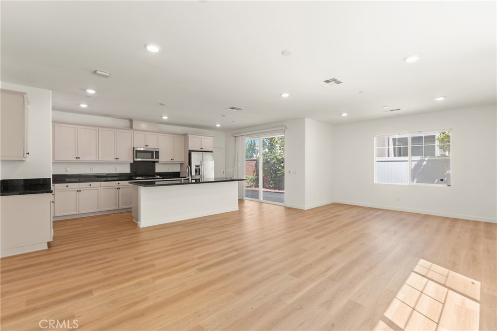 Vacant open-plan kitchen with white cabinets, a black-countertop peninsula, and light wood floors.