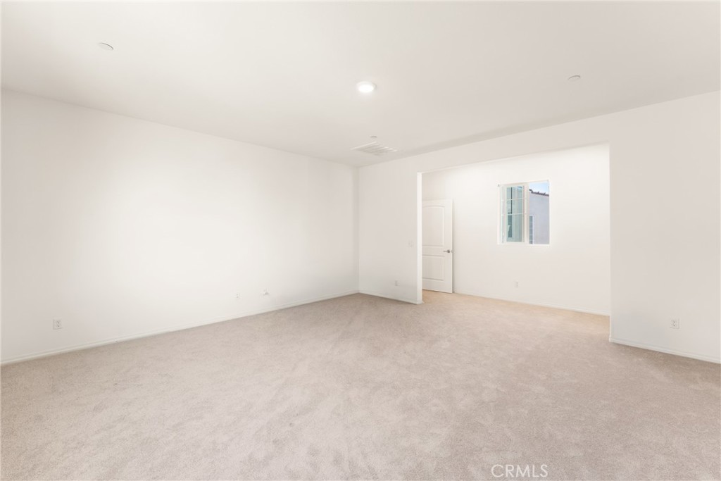 Empty carpeted room with white walls and a wide opening to an adjoining room.