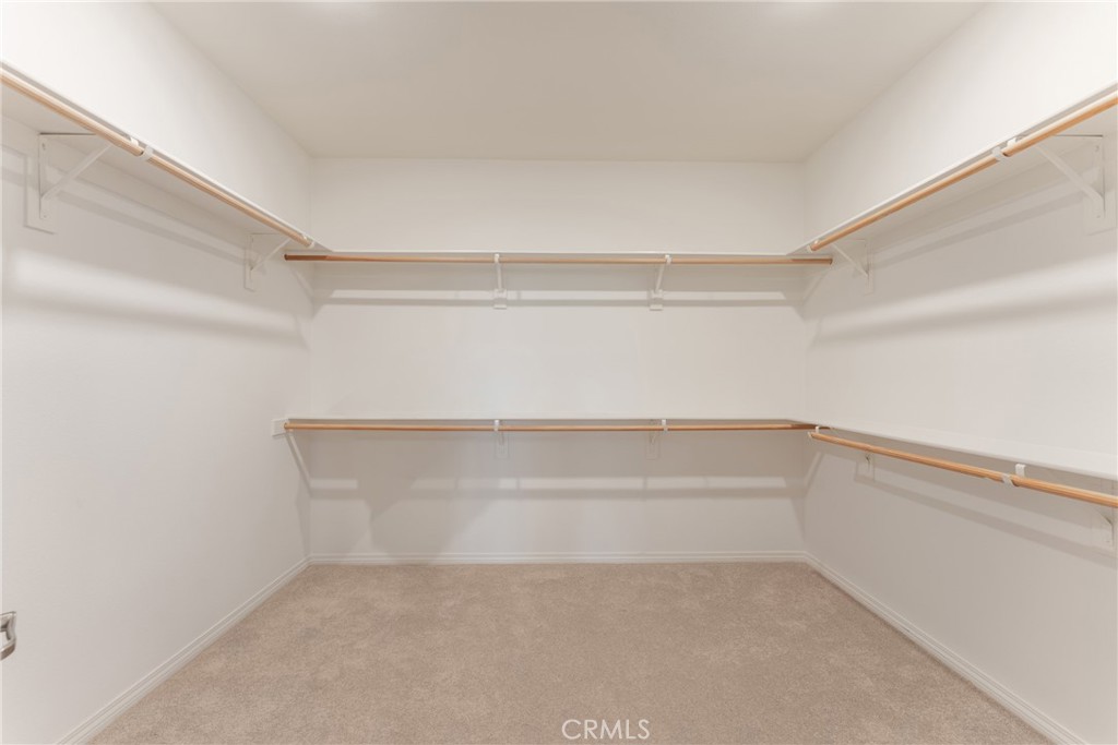 Empty walk-in closet with beige carpet and wooden hanging rods on three sides.