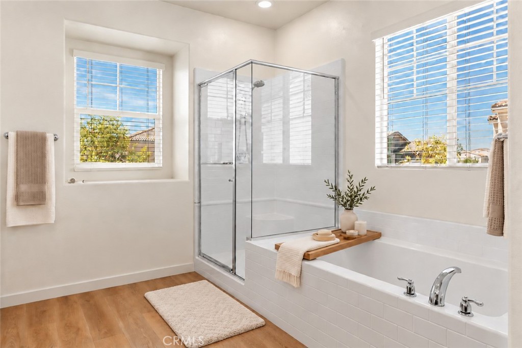 Bright bathroom with a glass-enclosed shower, bathtub, and two large windows.