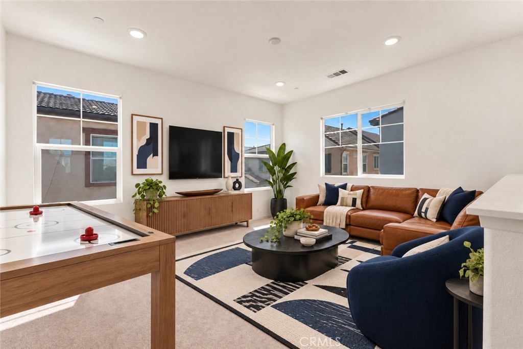 Staged living room with a brown leather sectional, navy armchairs, and large windows.