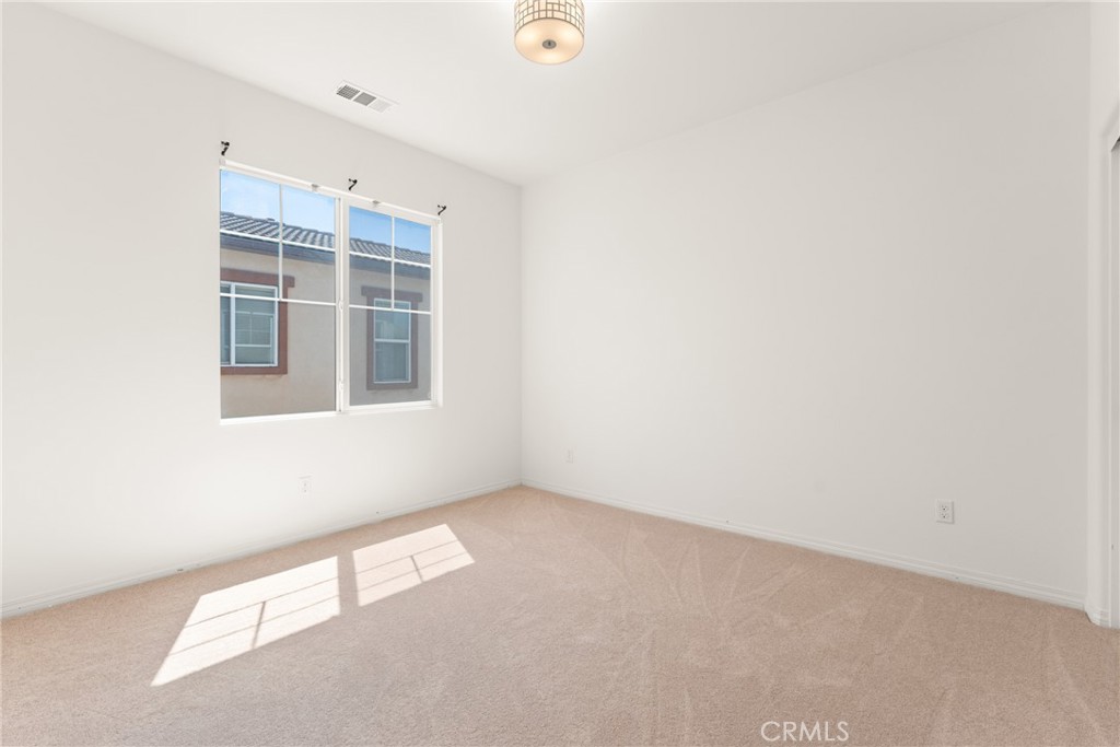 Empty bedroom with beige carpet, a ceiling light, and a sunlit window.