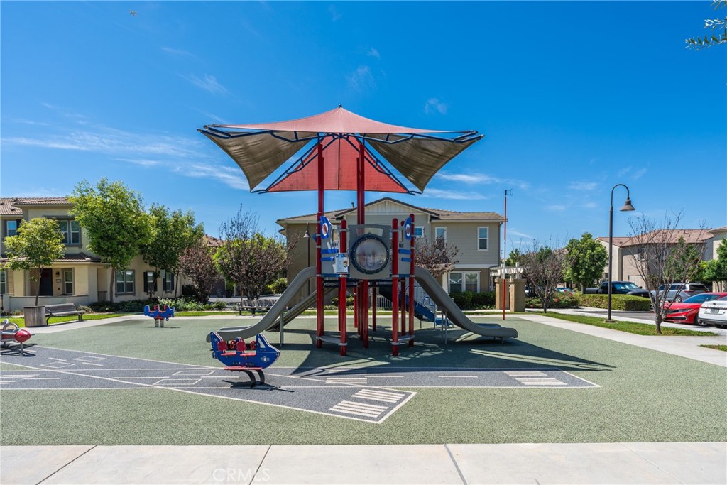 Neighborhood playground with a red-and-gray climbing structure and slides beneath a shade canopy.