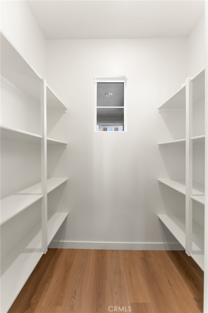 Walk-in closet with white built-in shelves, wood flooring, and a small back-wall window.