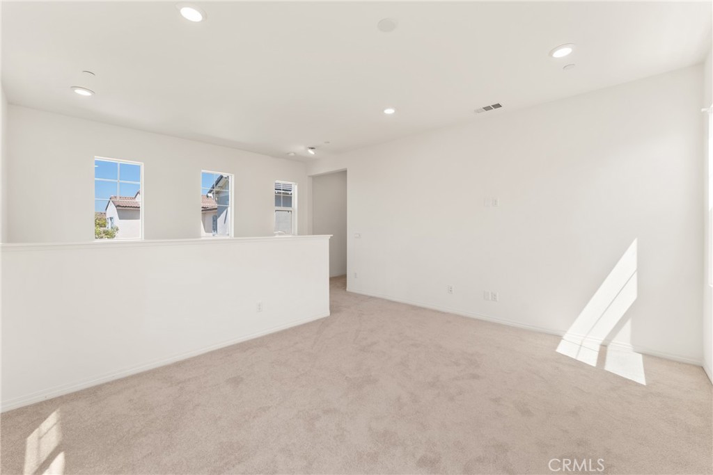 Empty carpeted room with recessed lights, windows above a half wall, and sunlight on the floor.