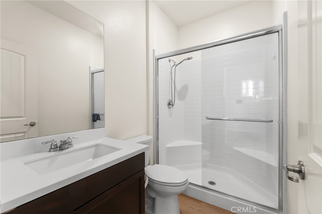 Bathroom with dark wood vanity and a spacious white-tiled shower behind glass.