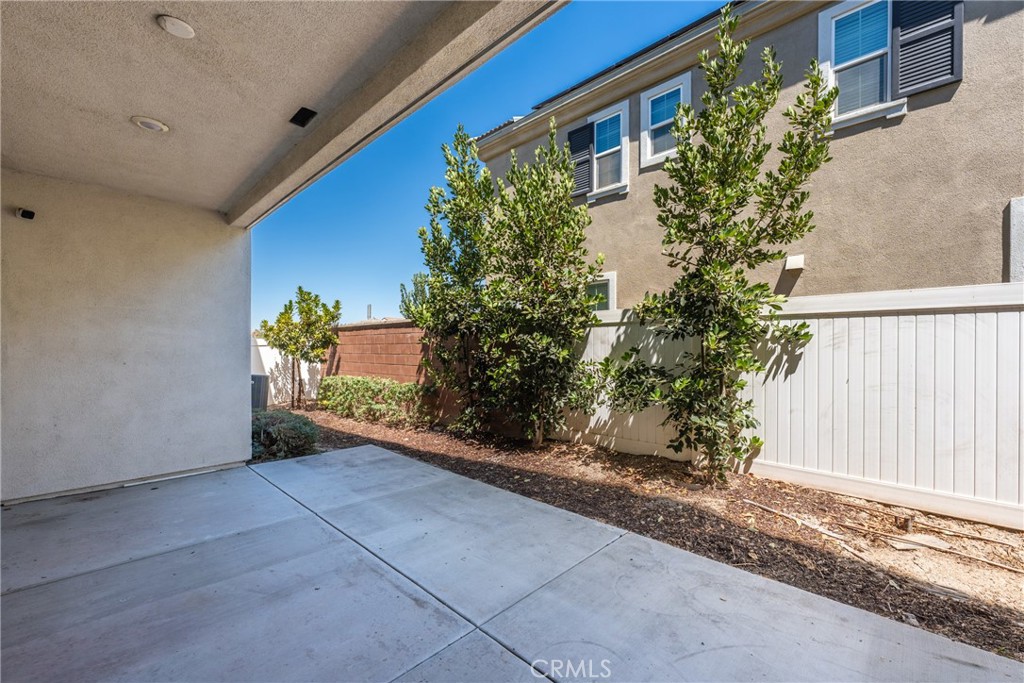 Covered concrete patio beside a landscaped side yard and white privacy fence.