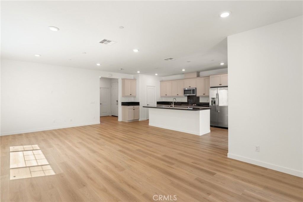 Open-plan living area and kitchen with light wood floors, pale cabinets, and stainless steel appliances.