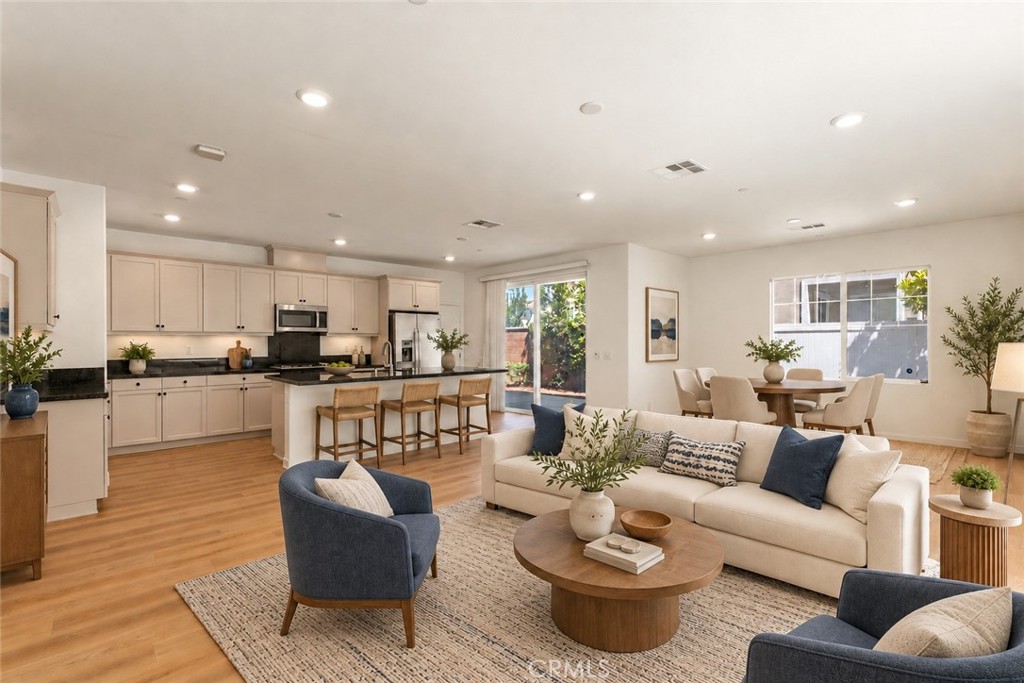 Open-plan living room with a cream sofa, round coffee table, kitchen island, and dining area.
