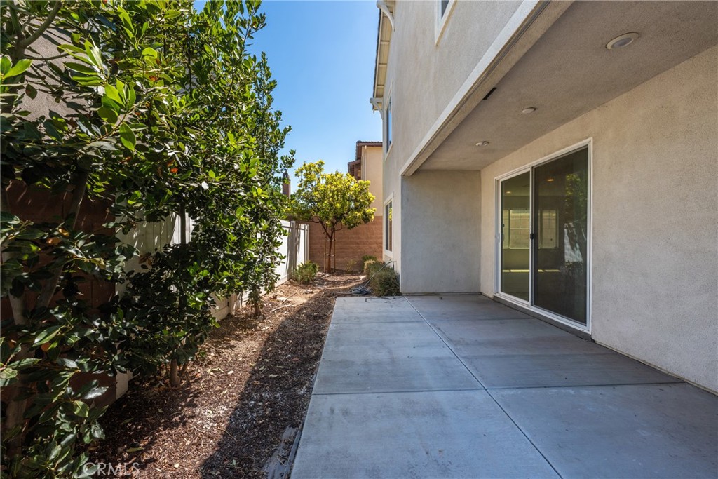 Concrete side patio beside a home, with a covered overhang, sliding glass door, and leafy landscaping.