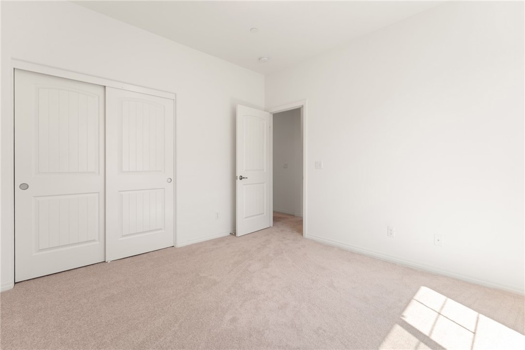 Empty bedroom with paneled closet doors and sunlight across the carpet.