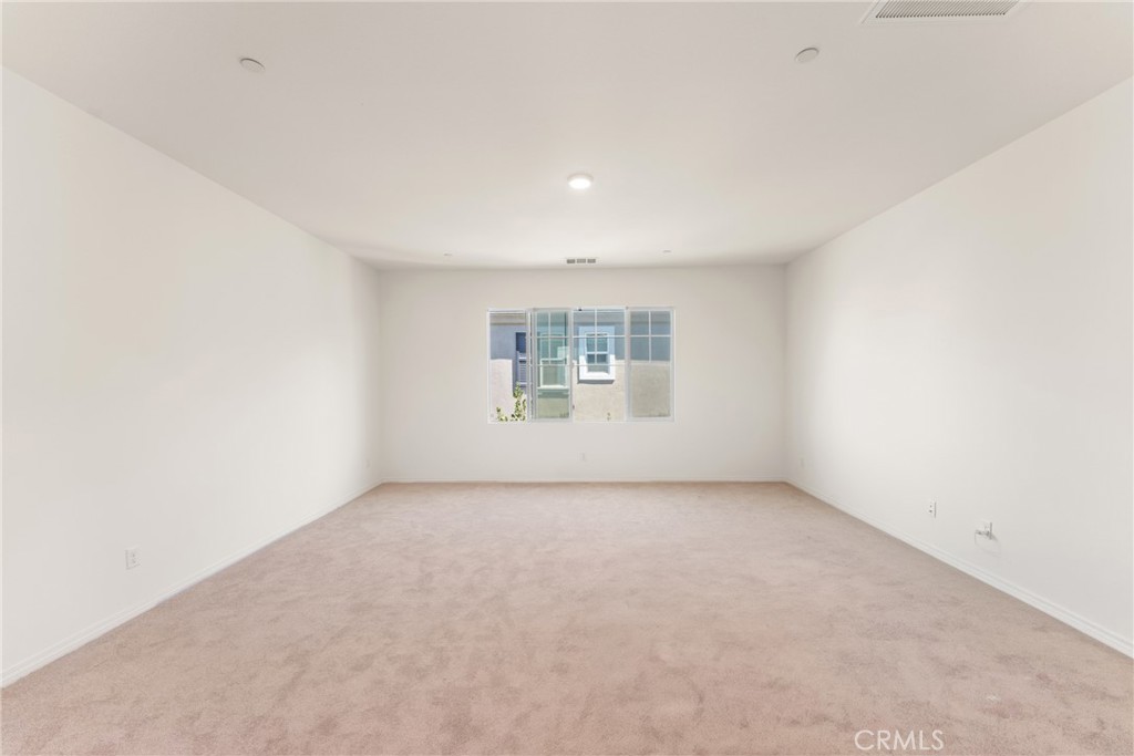 Empty bedroom with beige carpet, a centered window, and recessed ceiling lights.