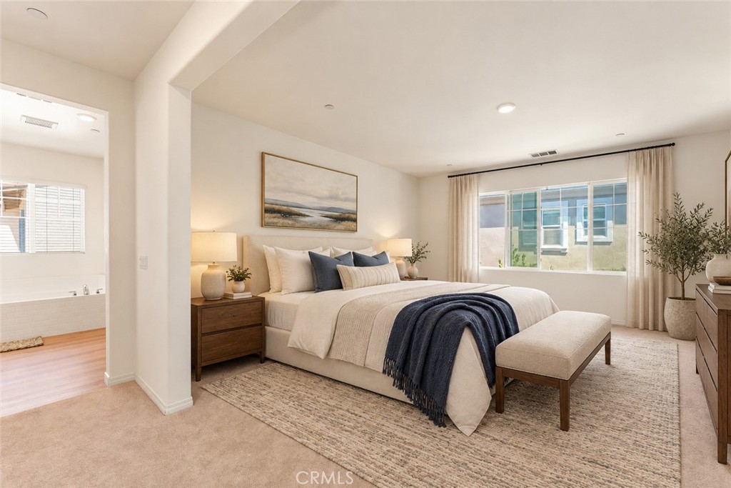 Staged primary bedroom with a king bed, navy throw, broad curtained window, and adjoining bathroom.