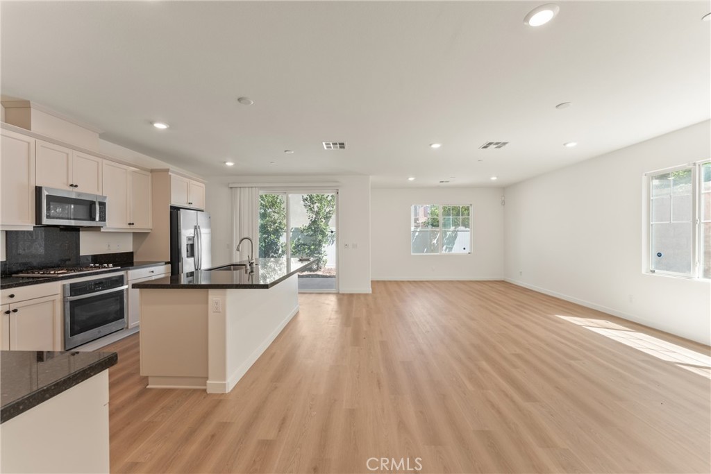 Open-plan kitchen and living area with a stone island, stainless appliances, and light wood floors.