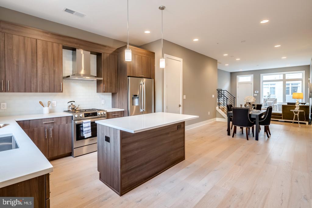 Open-plan kitchen with dark wood cabinets and a large white island leading to a dining area.