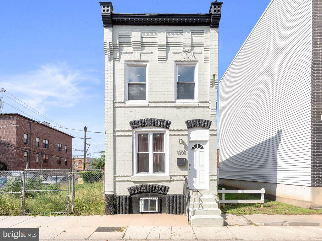 Narrow white brick house with dark trim, front steps, and a basement window.
