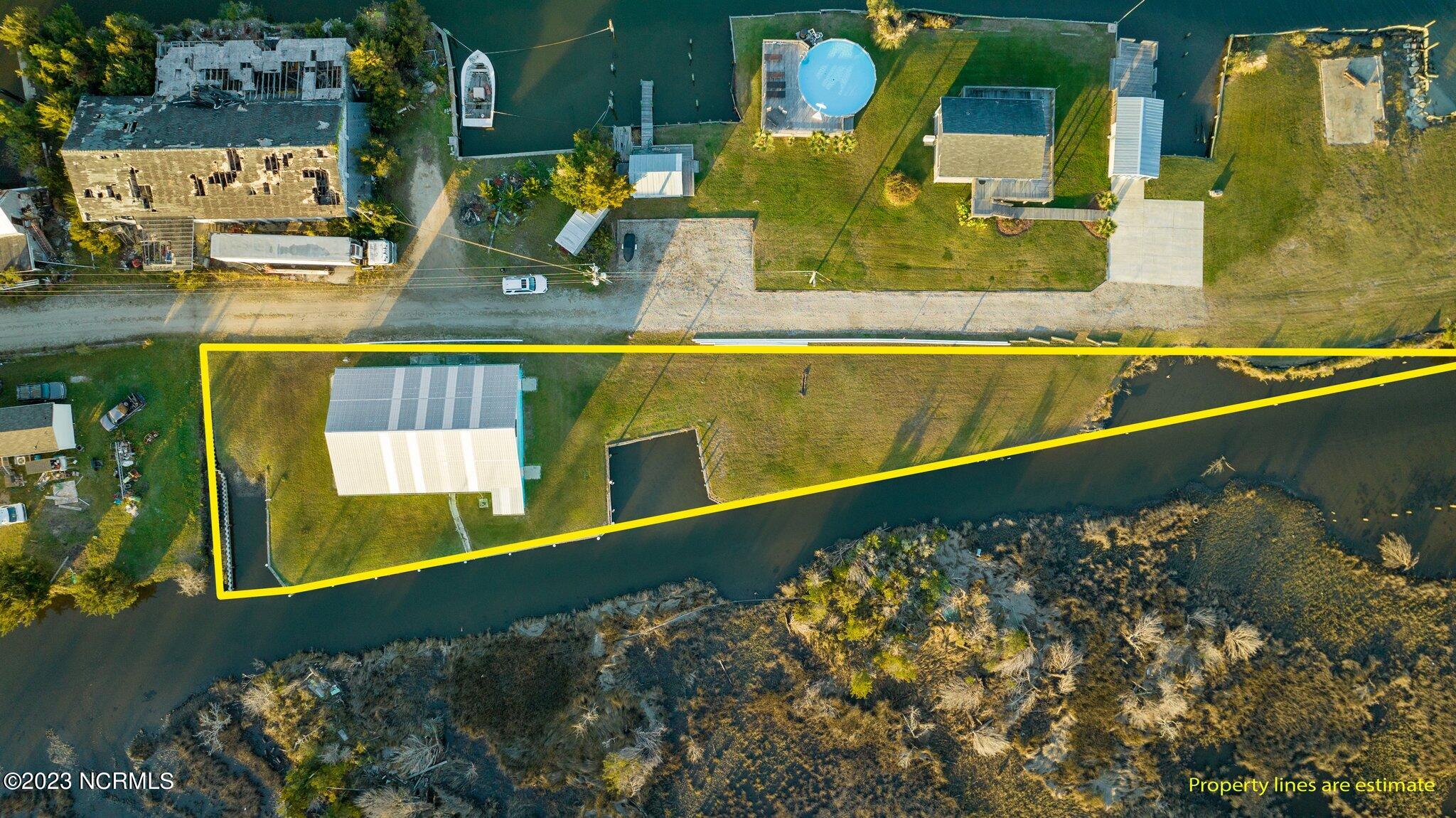 Aerial view of a canal-side lot outlined in yellow, with a large metal-roofed outbuilding.