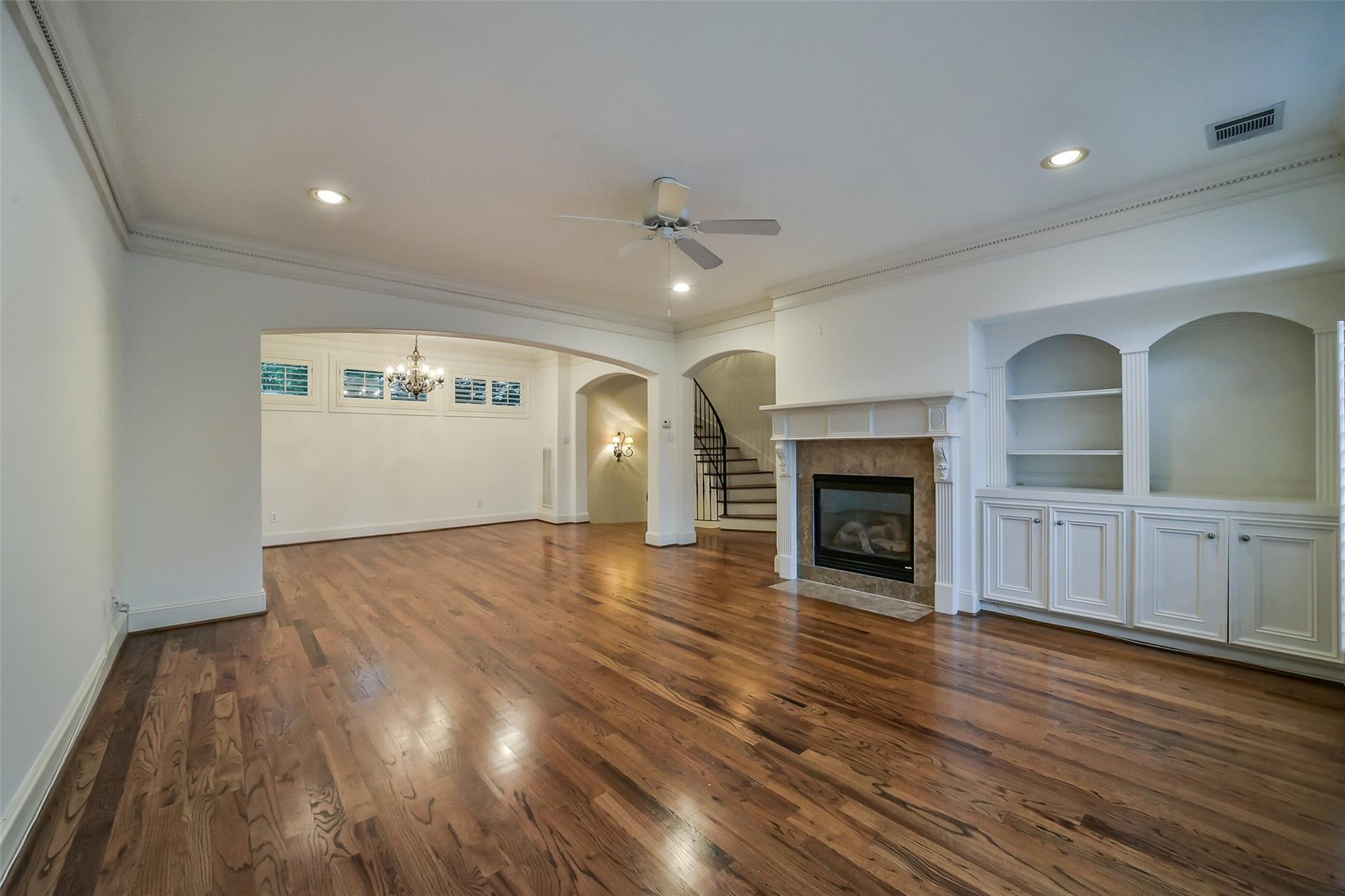 Unfurnished living room with hardwood floors, a fireplace, built-in shelving, and a curved staircase.