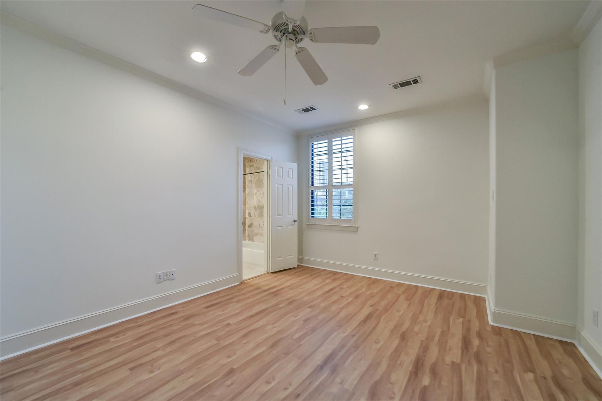 Empty bedroom with light wood floors, a ceiling fan, and a shuttered window.