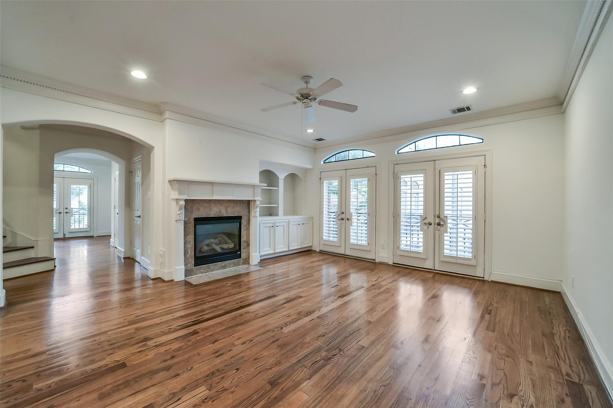 Vacant living room with hardwood floors, a fireplace, and plantation-shuttered French doors.