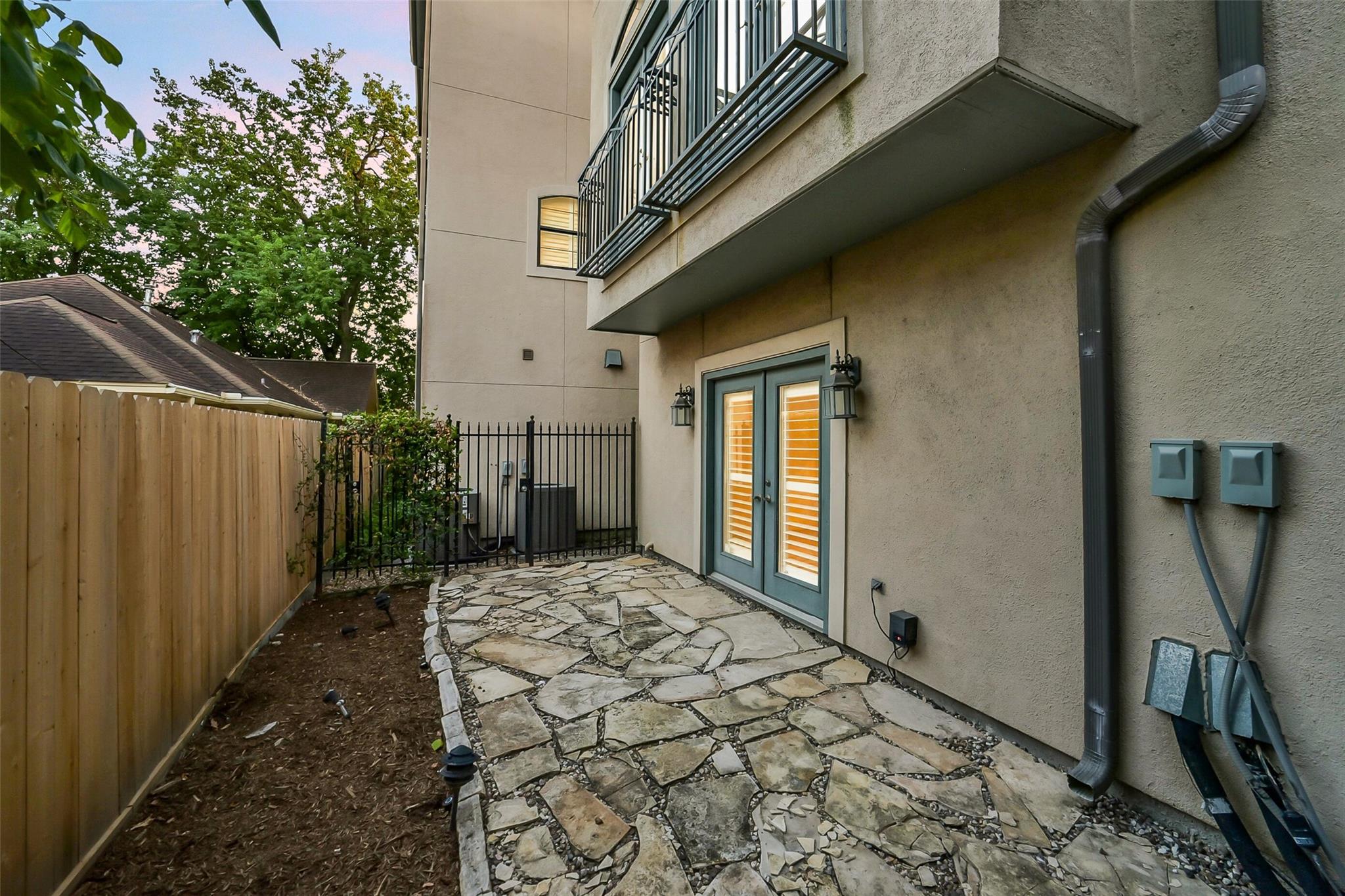 Rear patio with irregular stone paving, louvered double doors, and a metal-railed balcony.