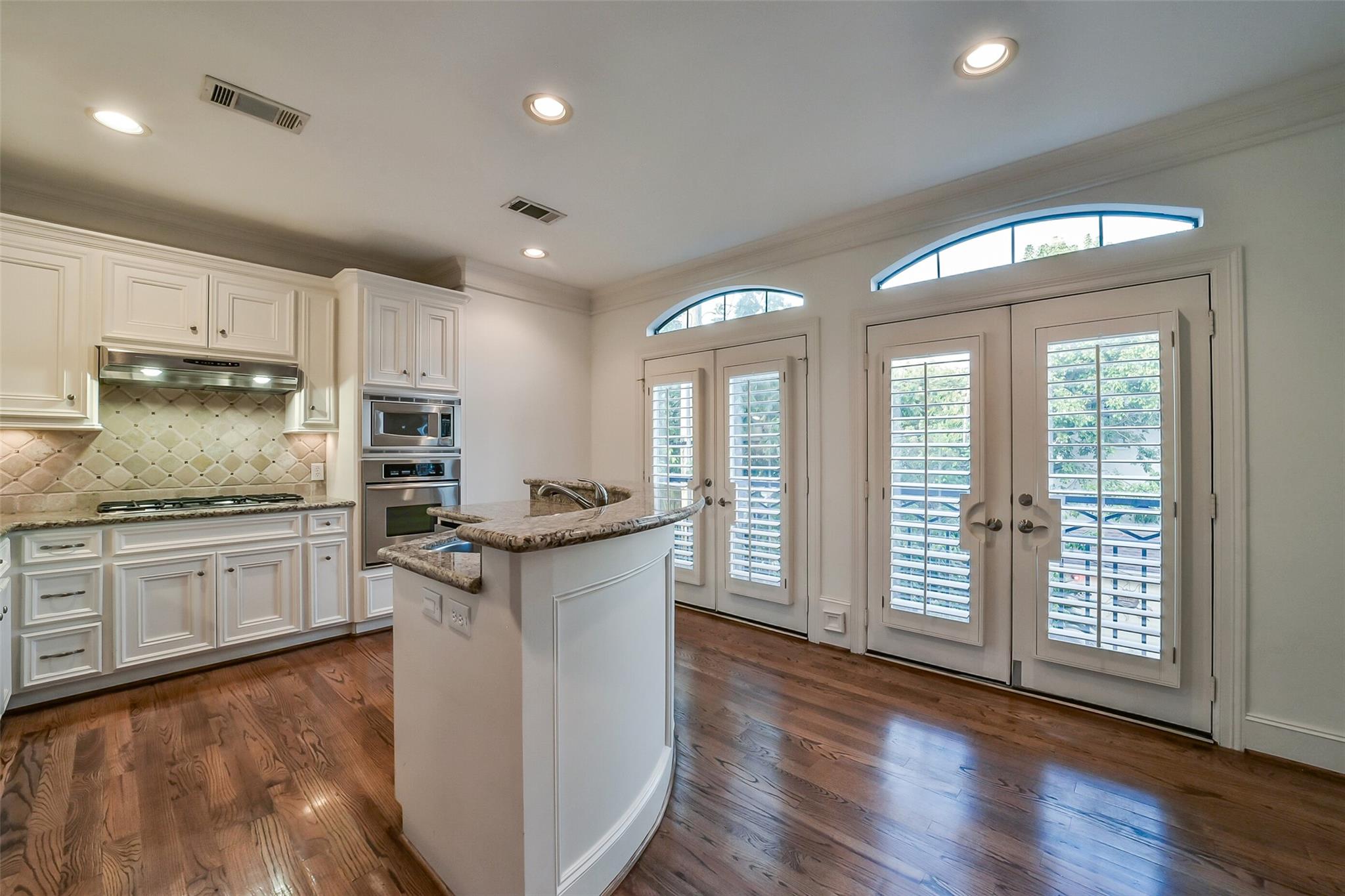 Kitchen with a granite-topped island, white cabinets, and shuttered French doors.