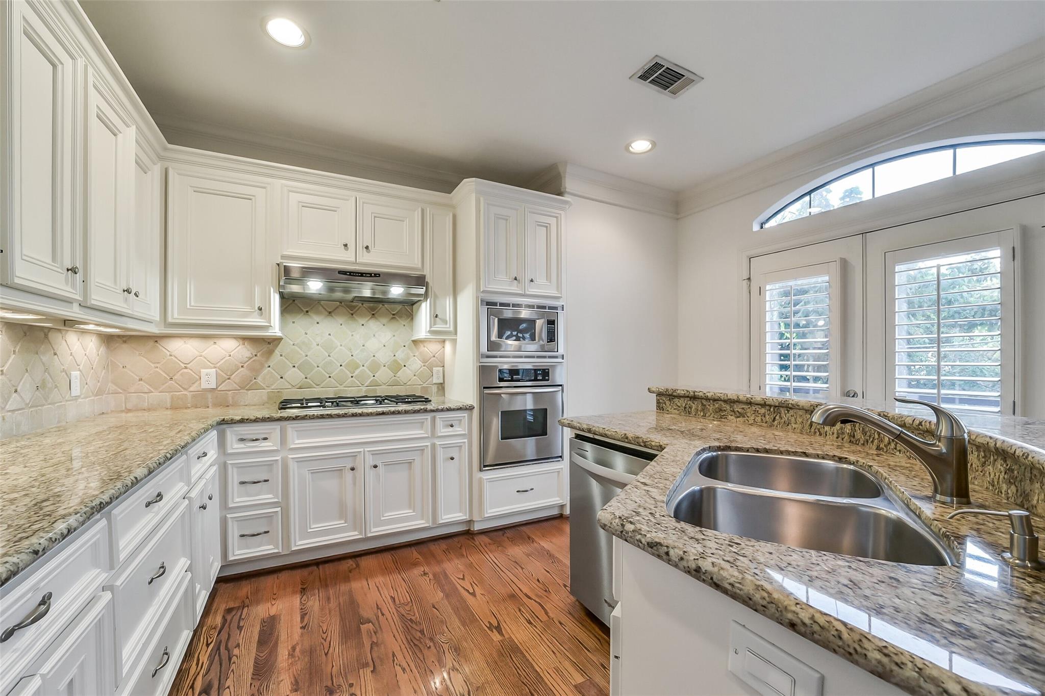Kitchen with white cabinetry, granite counters, a double sink, stainless appliances, and shuttered French doors.