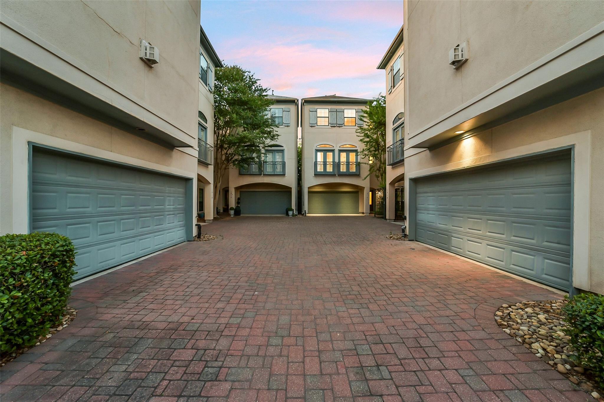 Attached homes with blue-gray garage doors around a brick-paved courtyard at dusk.