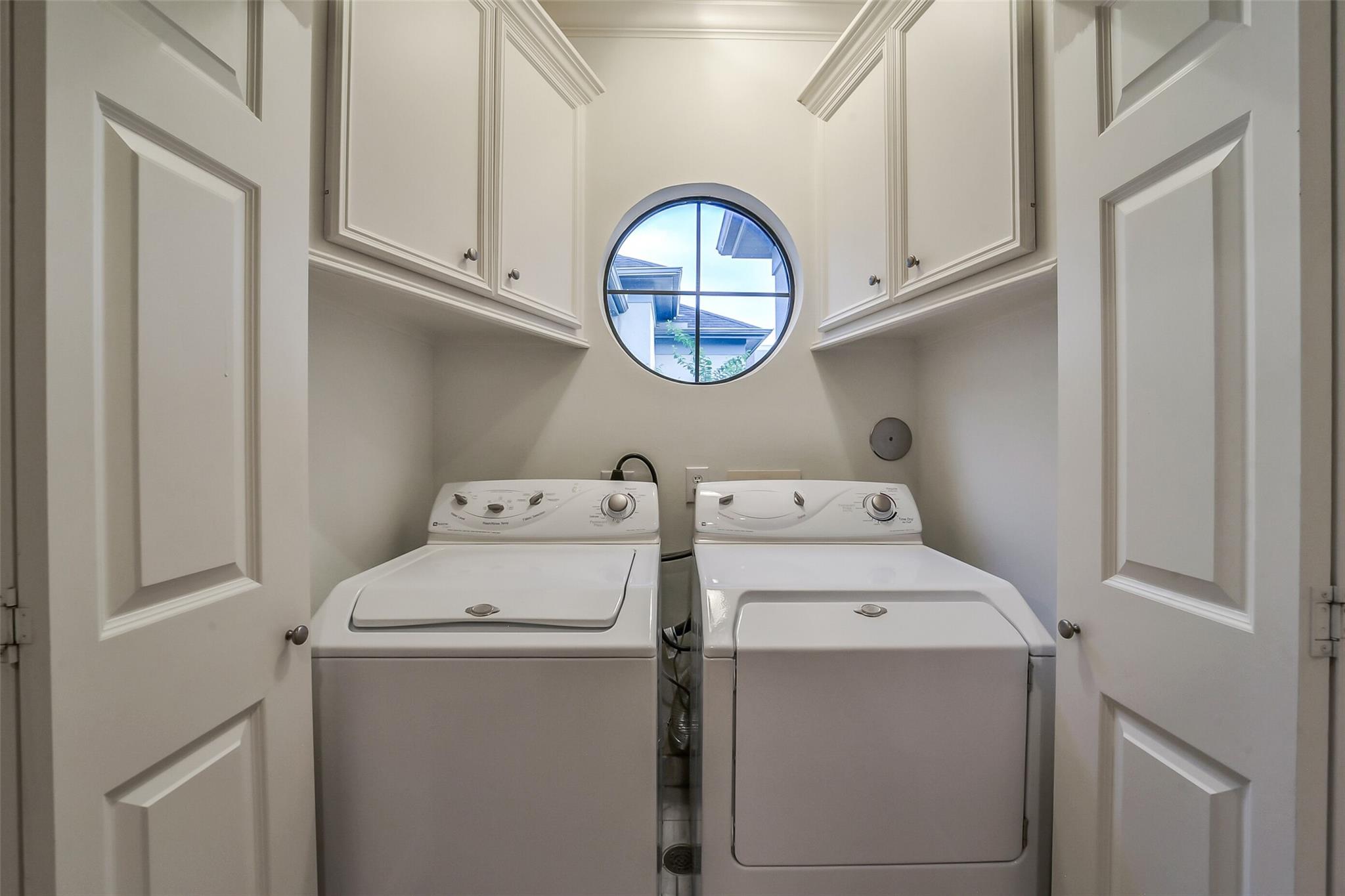 Laundry room with washer and dryer beneath built-in cabinets and a round window.